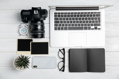 Photo of Flat lay composition with laptop, camera and smartphone on white wooden table. Designer's workplace