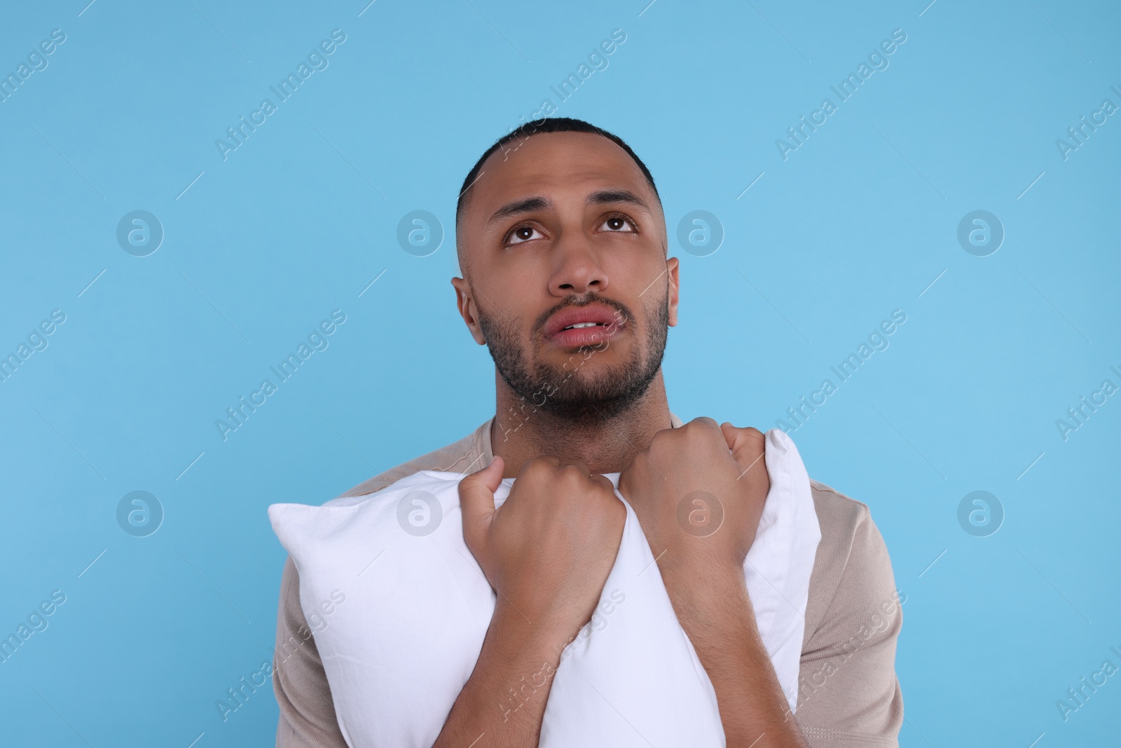 Photo of Tired man with pillow on light blue background. Insomnia problem