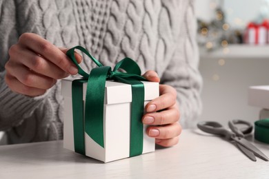 Photo of Woman decorating gift box at white table, closeup. Christmas present