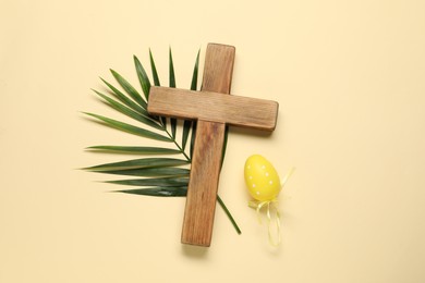 Photo of Wooden cross, painted Easter egg and palm leaf on beige background, top view