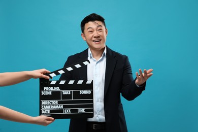 Photo of Happy asian actor performing while second assistant camera holding clapperboard on light blue background. Film industry