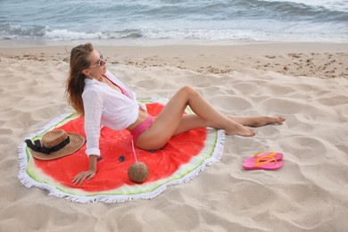 Beautiful woman sitting on beach towel near sea