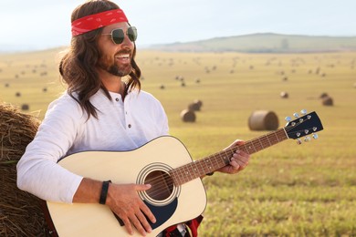 Photo of Hippie man playing guitar near hay bale in field