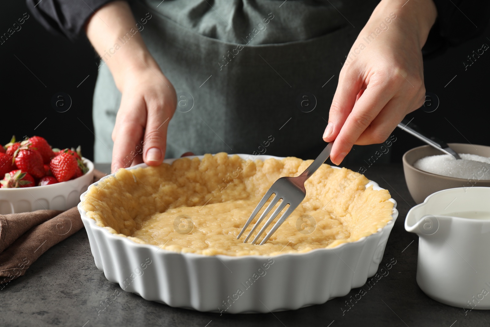 Photo of Shortcrust pastry. Woman making holes in raw dough with fork at grey table, closeup