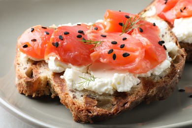 Delicious sandwich with cream cheese, salmon and black sesame seeds on grey plate, closeup