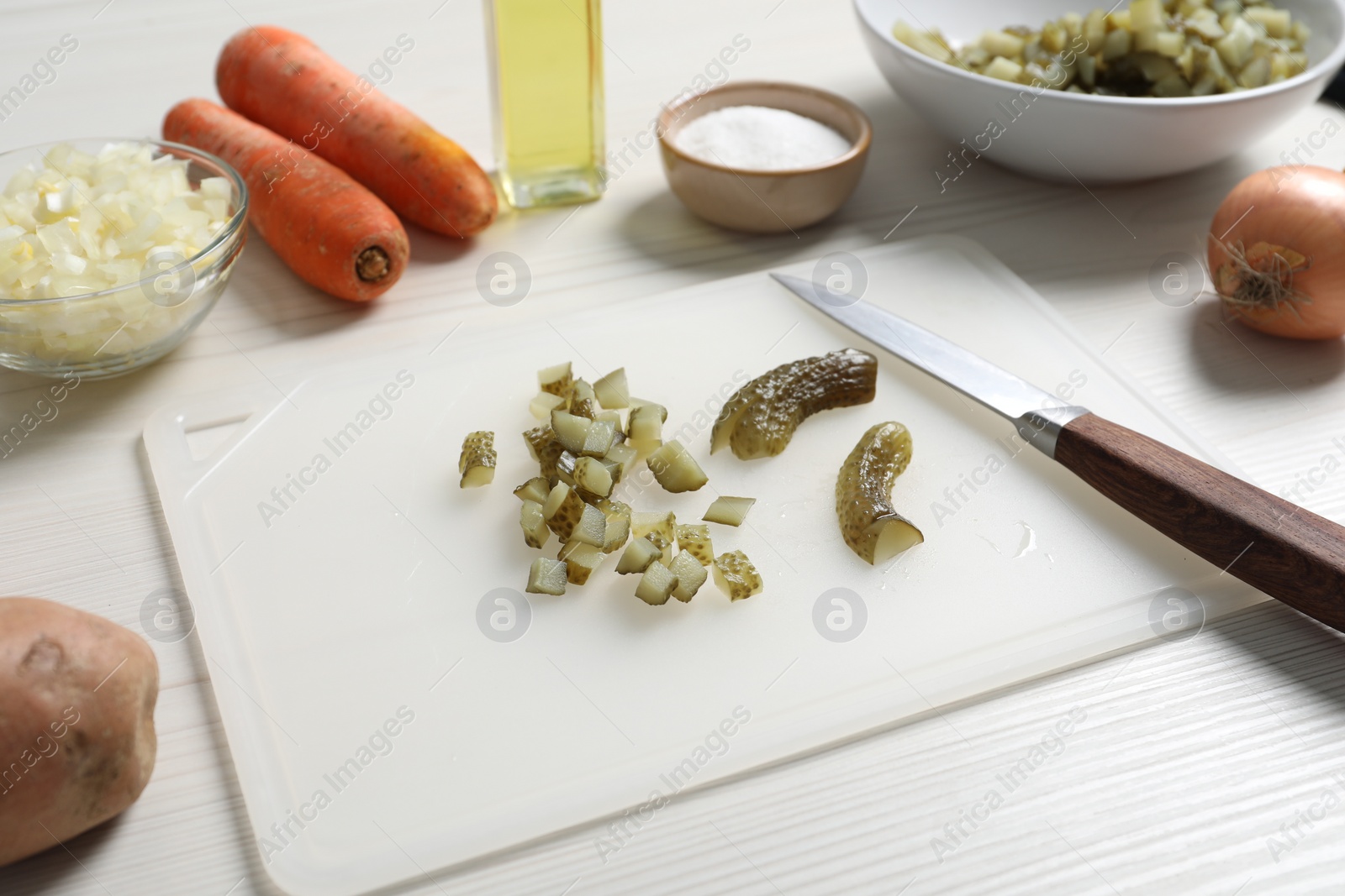 Photo of Cut pickled cucumbers and ingredients on white wooden table. Cooking vinaigrette salad