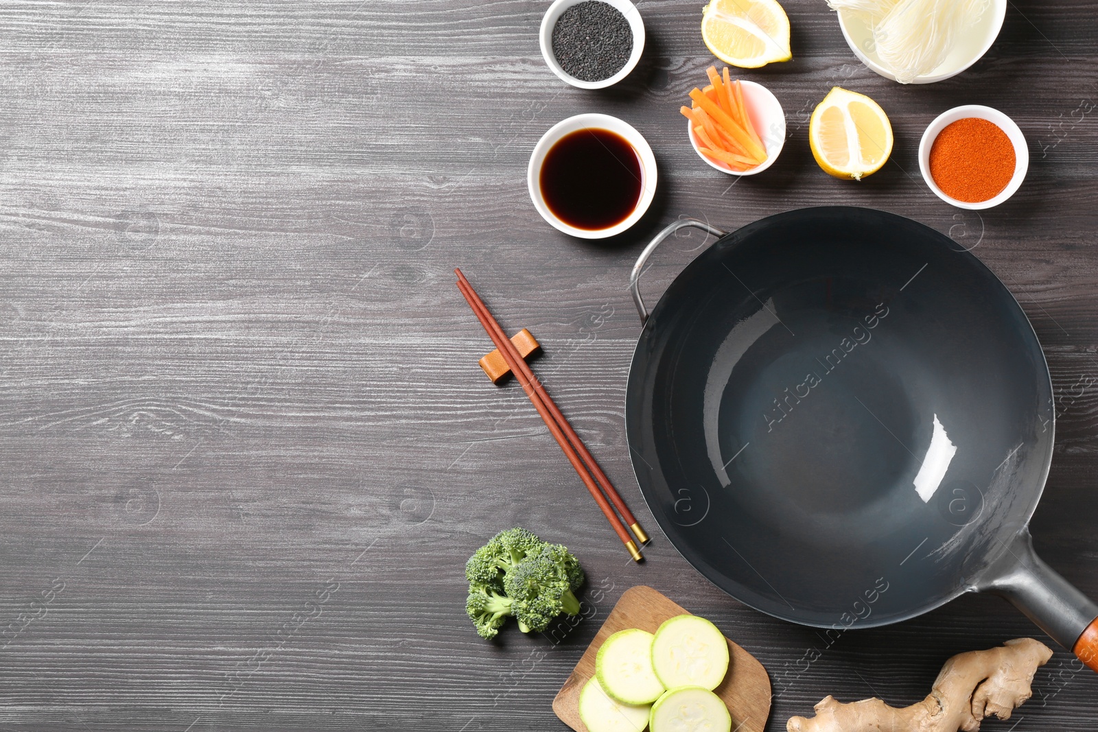 Photo of Empty iron wok, chopsticks and ingredients on grey wooden table, flat lay. Space for text