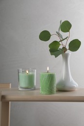 Scented candles near vase with eucalyptus branch on wooden table