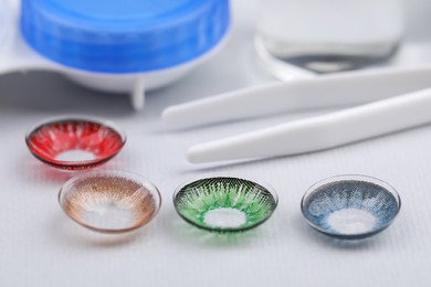Photo of Different color contact lenses and tweezers on white background, closeup