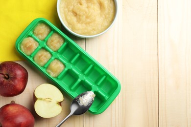 Photo of Apple puree in ice cube tray ready for freezing with fresh apple fruits on wooden table, flat lay. Space for text