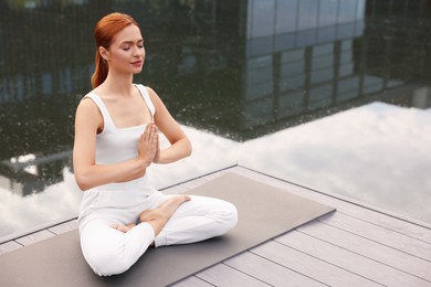 Beautiful young woman practicing Padmasana on yoga mat outdoors, space for text. Lotus pose