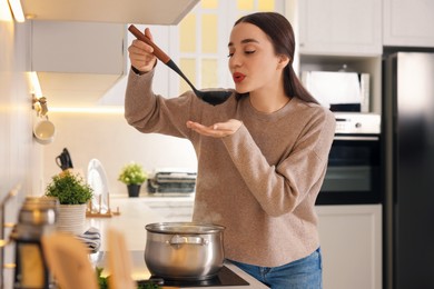 Photo of Beautiful woman with ladle tasting soup in kitchen