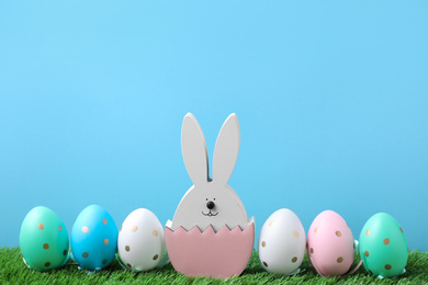 Photo of Easter bunny figure and dyed eggs on green grass against light blue background