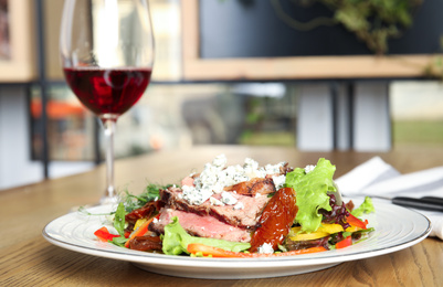 Photo of Delicious salad with roasted meat and vegetables served on wooden table indoors. Space for text