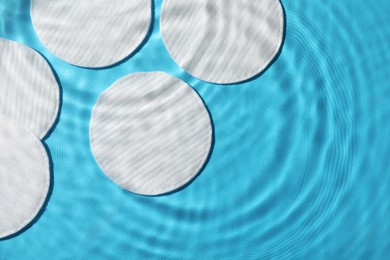 Photo of White cotton pads in water on light blue background, flat lay. Space for text