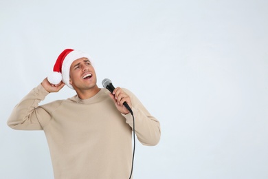 Photo of Emotional man in Santa Claus hat singing with microphone on white background, space for text. Christmas music