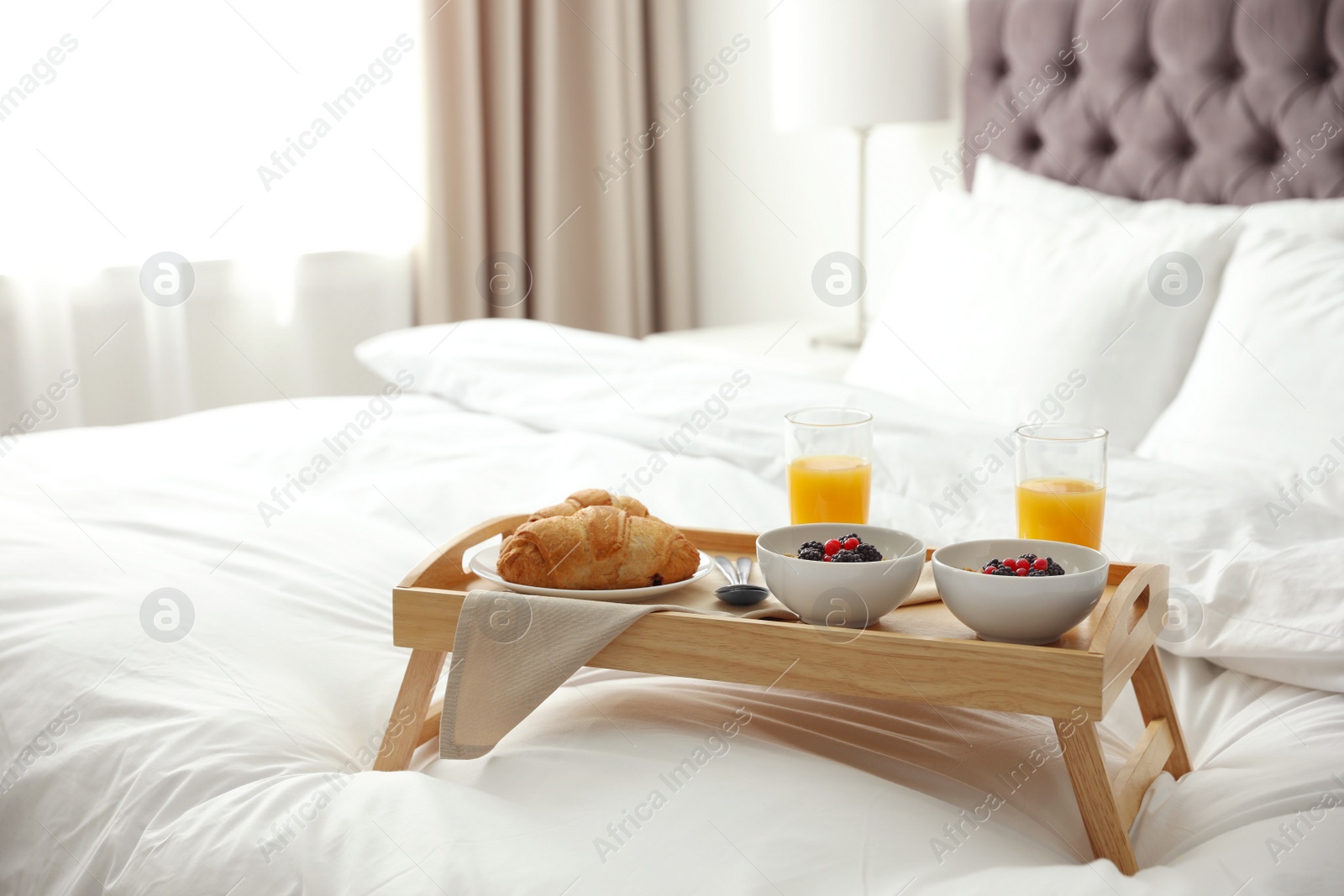 Photo of Tray with tasty breakfast on bed in light room