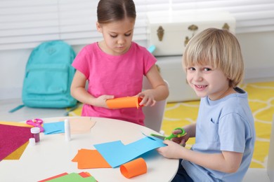 Photo of Cute children making paper toys at desk in room. Home workplace