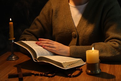 Photo of Woman reading Bible at table with burning candles, closeup