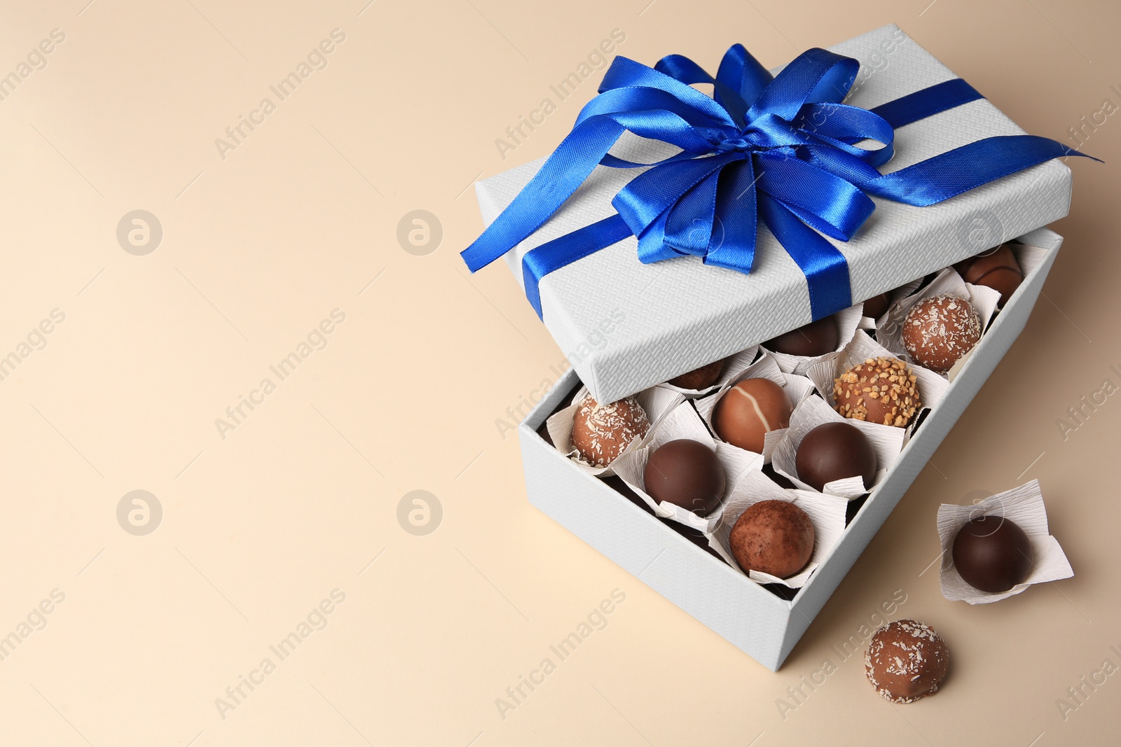 Photo of Box with delicious chocolate candies on beige background. Space for text