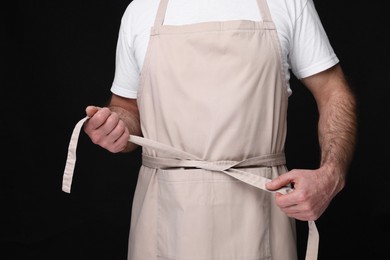 Man wearing kitchen apron on black background, closeup. Mockup for design