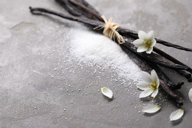 Photo of Vanilla pods, sugar, flowers and petals on gray textured table, closeup. Space for text