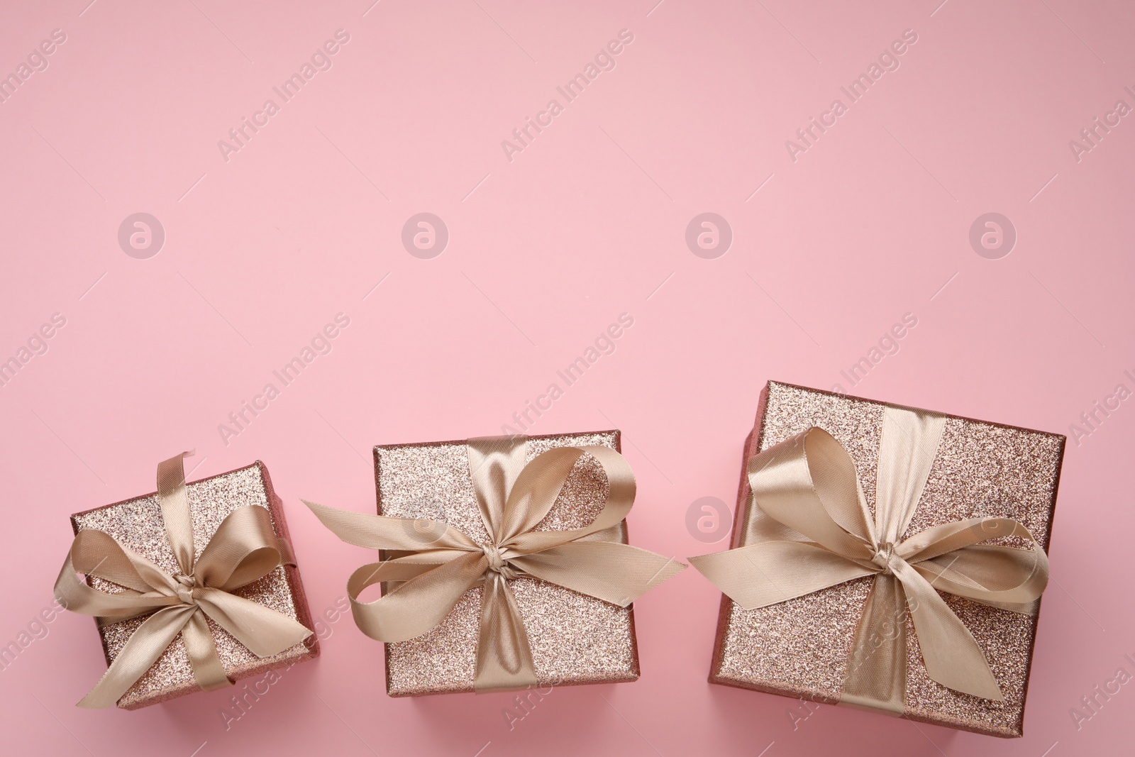 Photo of Shiny gift boxes with golden bows on pink background, flat lay. Space for text