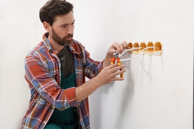 Professional electrician with pliers fixing wires indoors