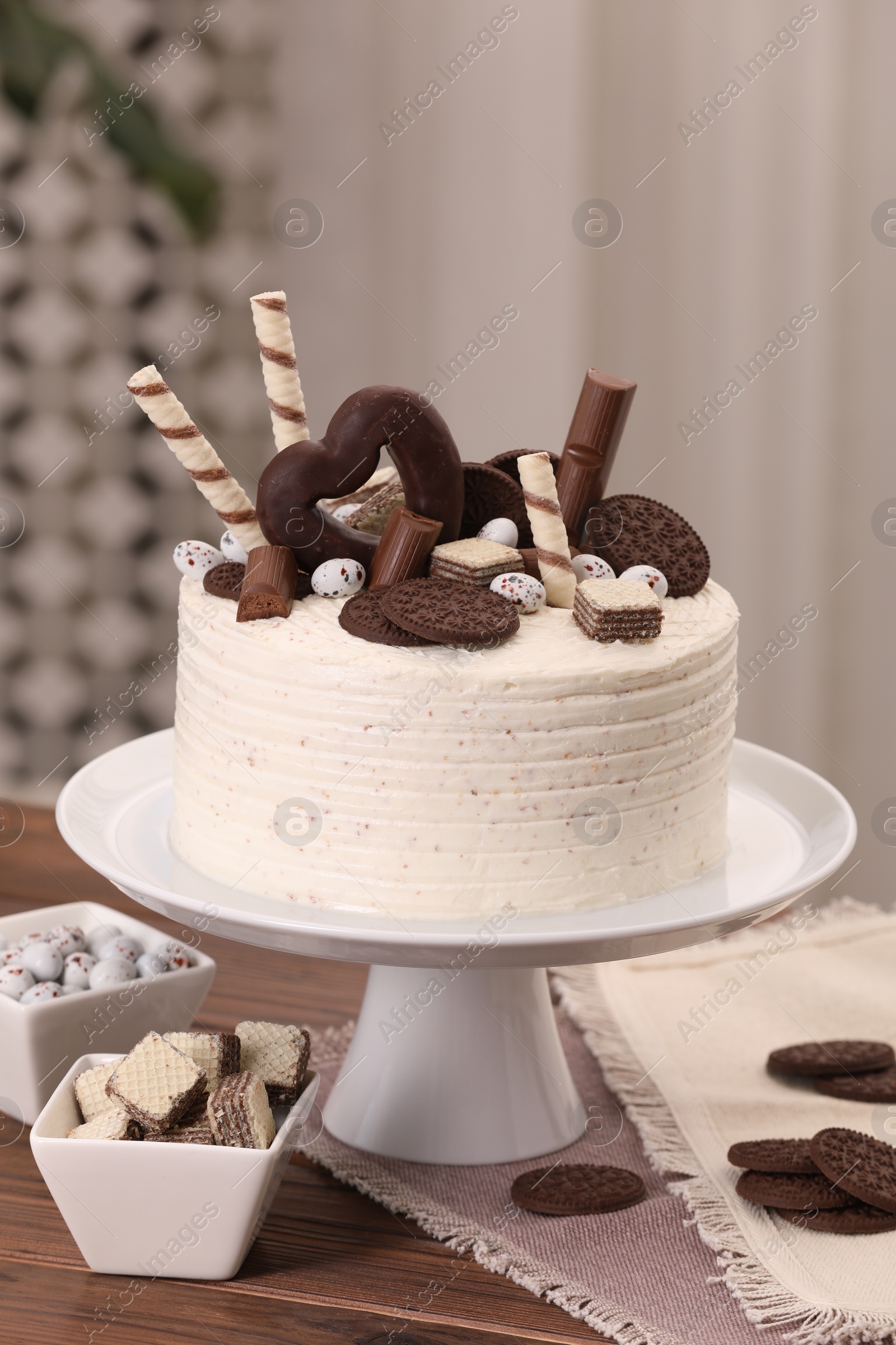 Photo of Delicious cake decorated with sweets on wooden table in kitchen