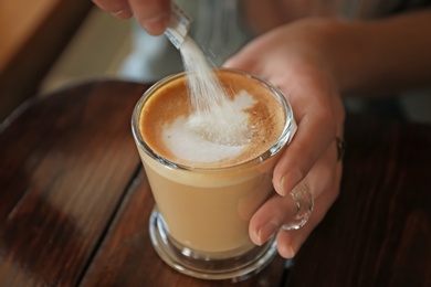 Woman adding sugar to aromatic coffee at wooden table