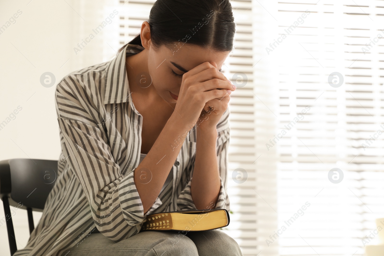 Photo of Beautiful young woman praying over Bible at home