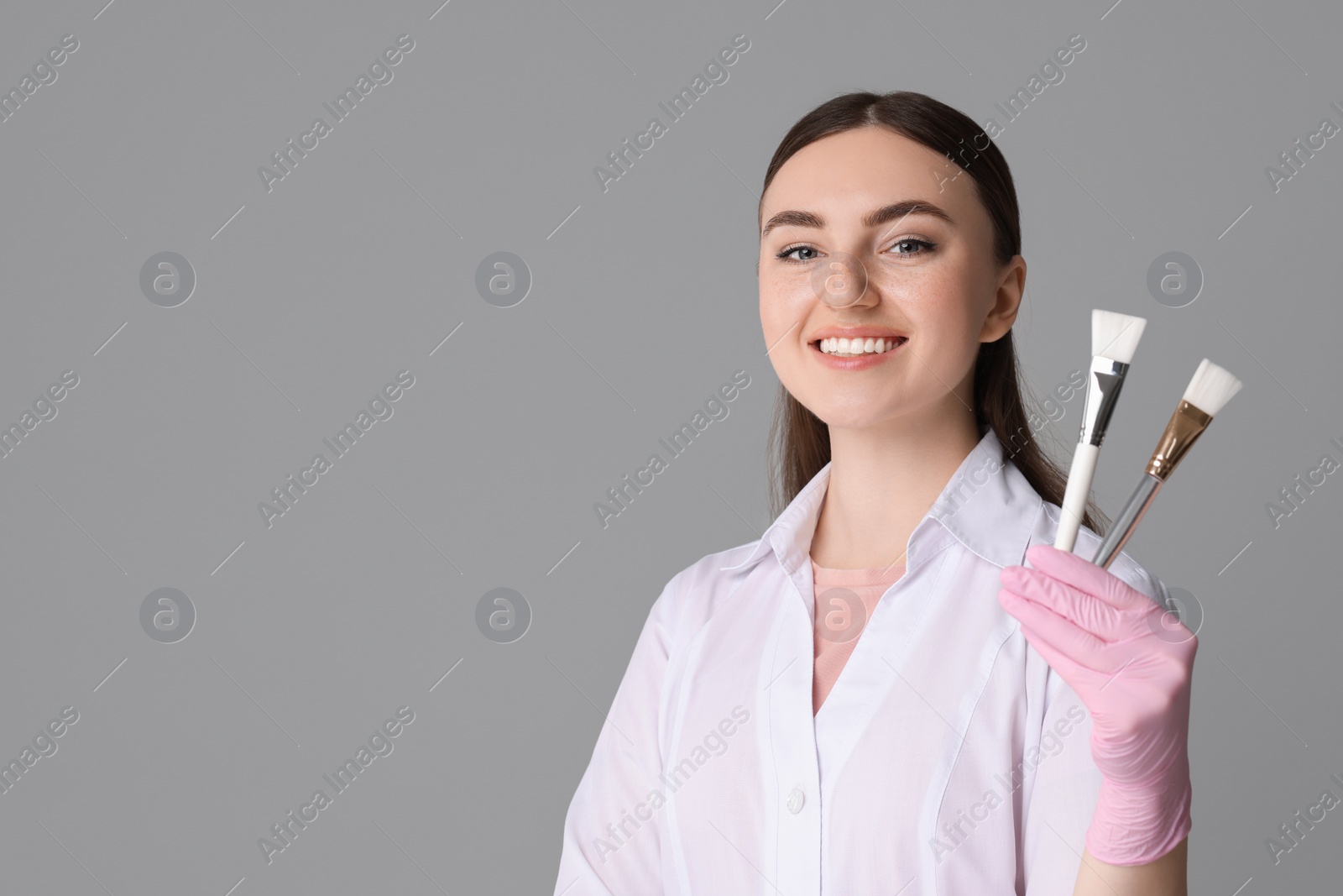 Photo of Cosmetologist with cosmetic brushes on grey background, space for text