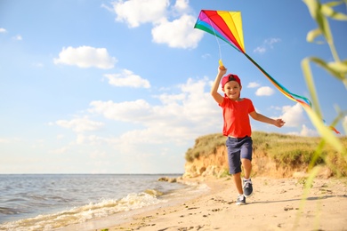 Photo of Cute little child with kite running on beach near sea. Spending time in nature