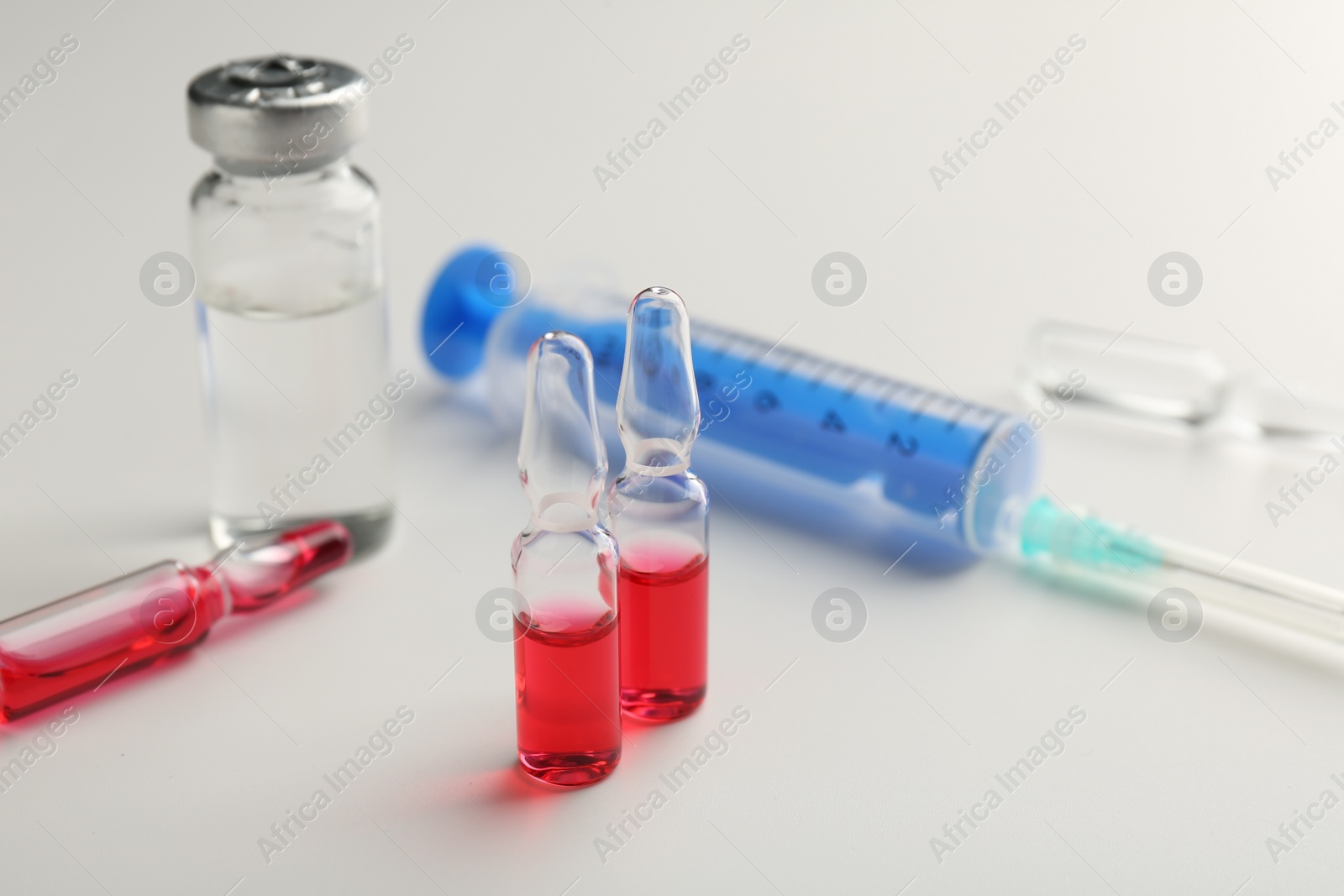 Photo of Glass ampoules with liquid and syringe on white background, closeup