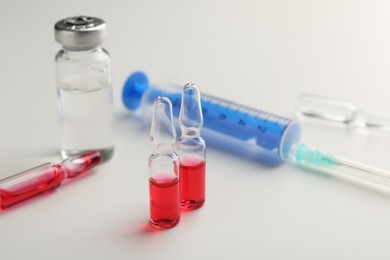 Glass ampoules with liquid and syringe on white background, closeup