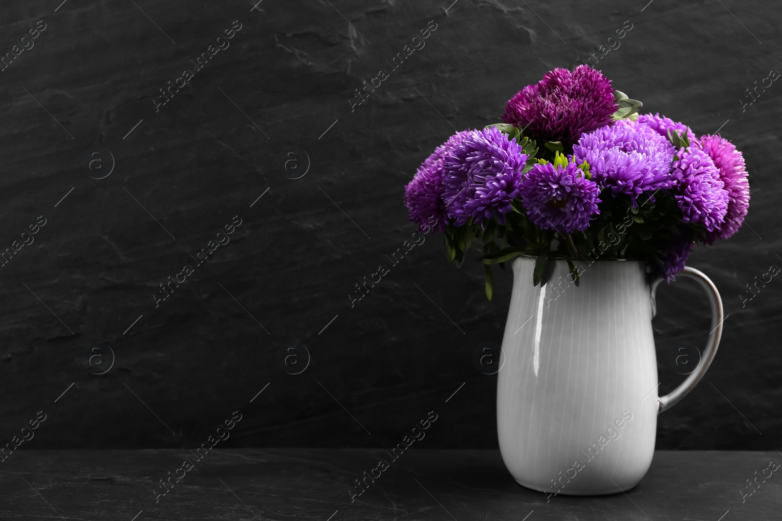 Photo of Beautiful asters in jug on table against black background, space for text. Autumn flowers