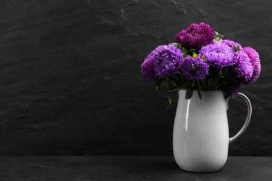 Photo of Beautiful asters in jug on table against black background, space for text. Autumn flowers