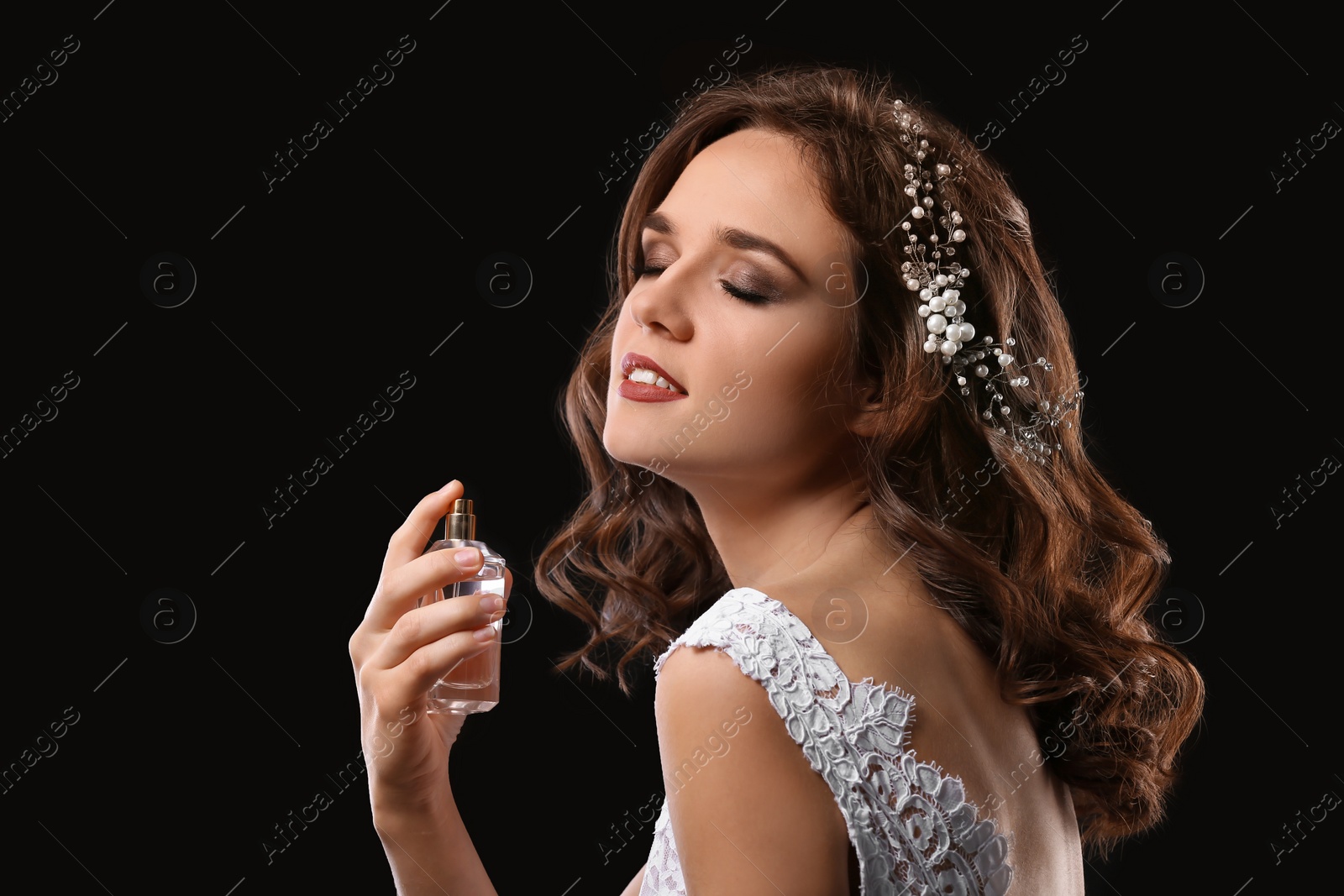 Photo of Beautiful young bride with bottle of perfume on black background