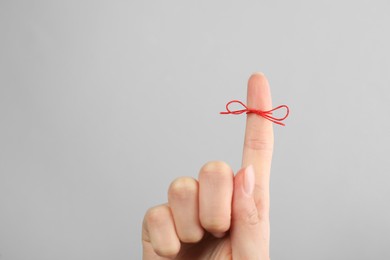 Photo of Woman showing index finger with tied red bow as reminder on light grey background, closeup