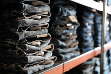 Photo of Collection of modern jeans on shelf in shop, closeup