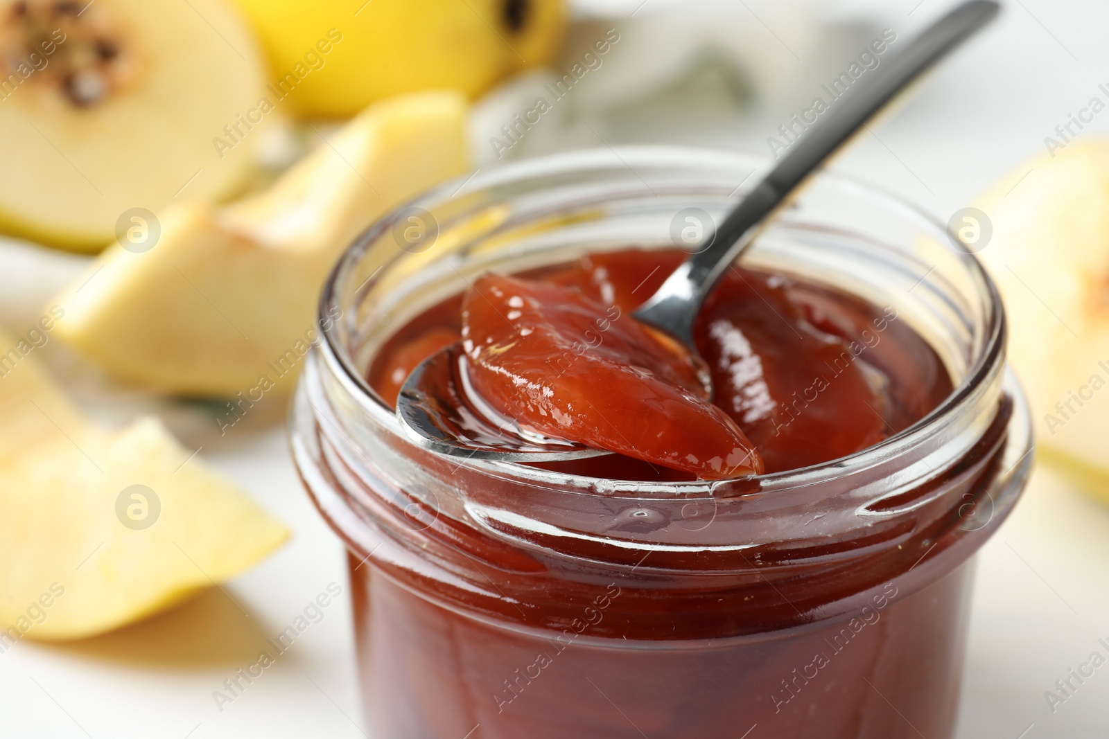 Photo of Taking tasty homemade quince jam from jar at table, closeup