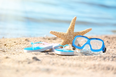 Photo of Starfish, goggles and flip flops on sand near sea. Beach object