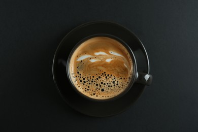 Cup of tasty coffee on black background, top view