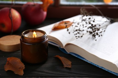 Photo of Beautiful burning candle and book on wooden table, closeup. Autumn atmosphere