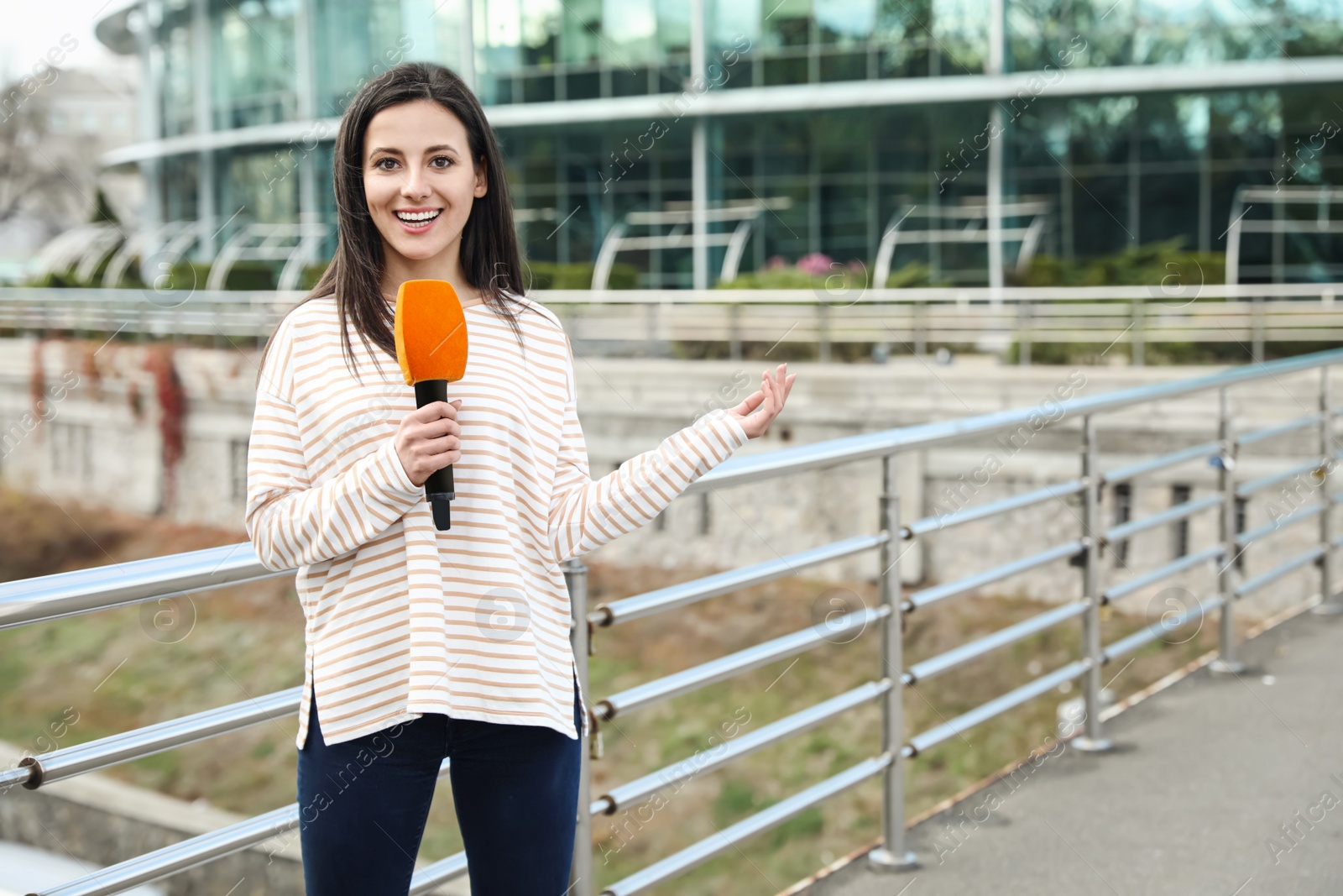 Photo of Young female journalist with microphone working on city street. Space for text