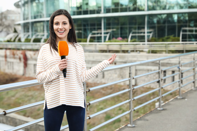 Young female journalist with microphone working on city street. Space for text