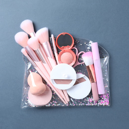 Plastic cosmetic bag with makeup products and beauty accessories on blue-gray background, top view