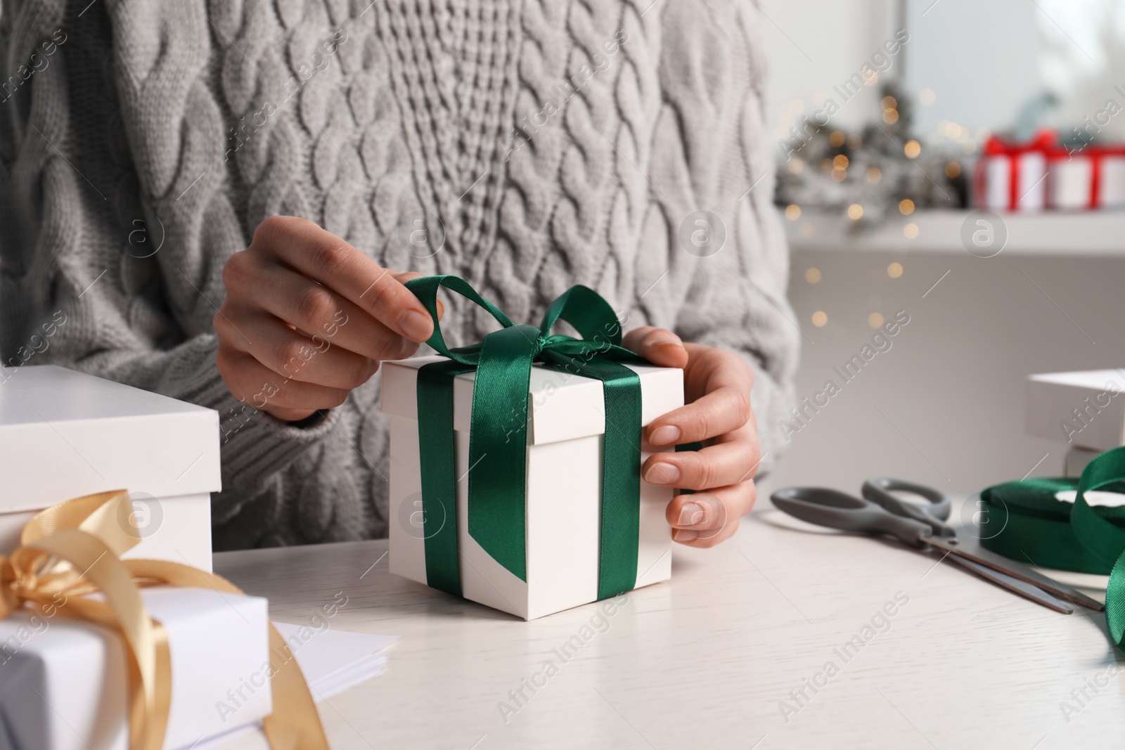 Photo of Woman decorating gift box at white table, closeup. Christmas present