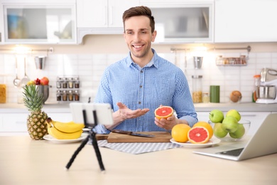 Photo of Young blogger with fruits recording video on kitchen