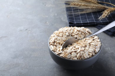 Photo of Oatmeal and spoon in bowl on grey table. Space for text
